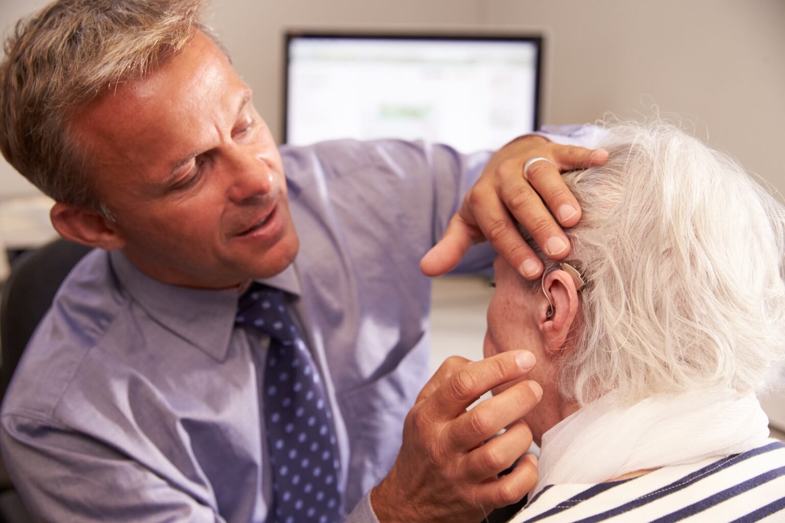 Audiologist Audiologist fitting a senior female patient with a hearing aid