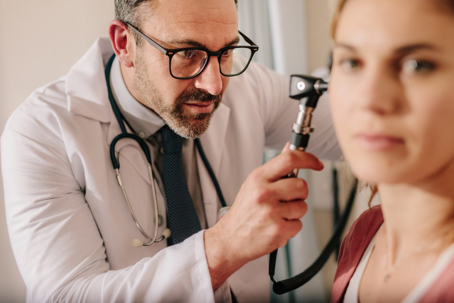 ENT doctor checking ear with otoscope of woman patient ENT doctor checking ear with otoscope of woman patient at hospital. Physician examining ear of female patient with an instrument.