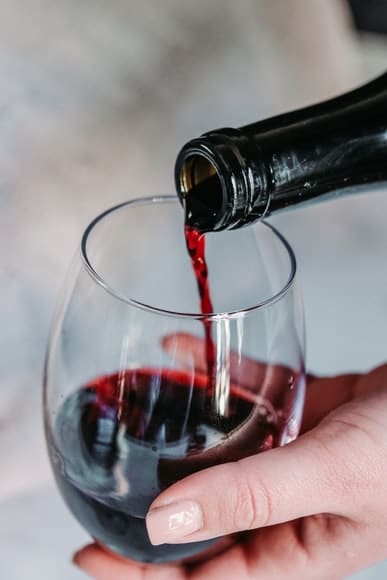 A bottle of red wine being poured into a glass.