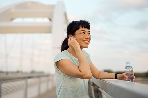Smiling woman out for a walk crossing a bridge and adjusting her hearing aids.